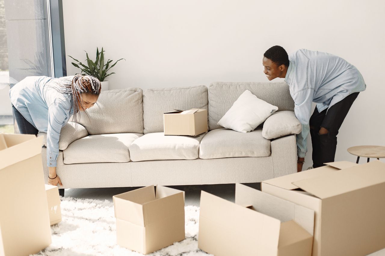 Un couple heureux installe un canapé dans sa nouvelle maison, entouré de cartons de déménagement.